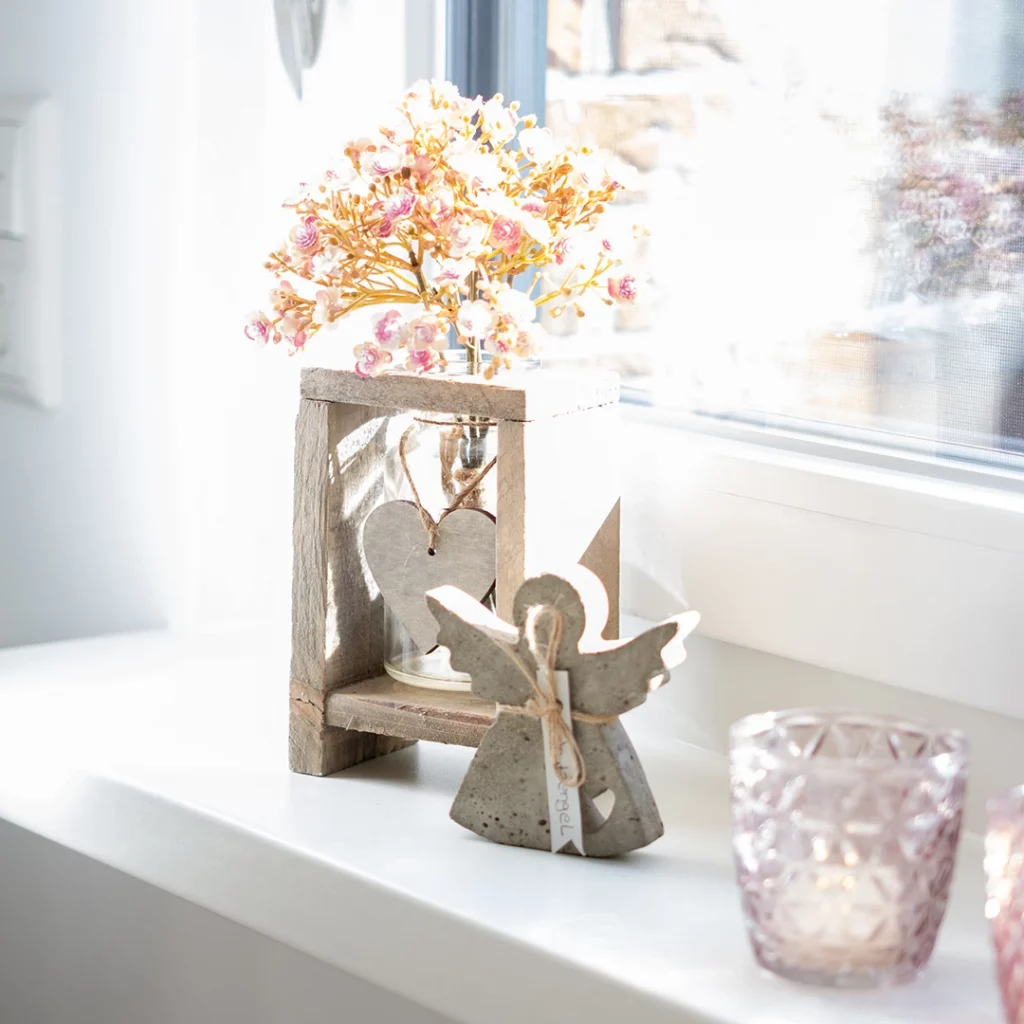 Auf der Fensterbank im Behandlungsraum stehen Teelichter, ein Schutzengel und eine Vase aus Beton mit Blumen.